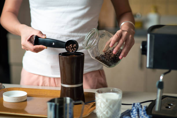 Woman inserting coffee beans into the grinder in the kitchen at home Woman inserting coffee beans into the grinder in the kitchen at home. Home barista and domestic lifestyle concept with unrecognizable person coffee grinder stock pictures, royalty-free photos & images