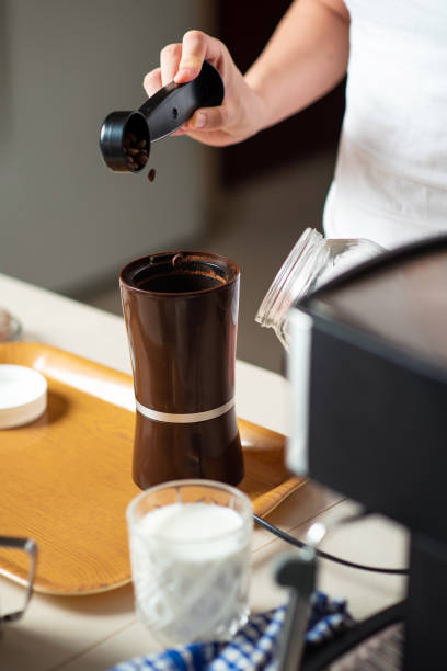istock Woman inserting coffee beans into the grinder in the kitchen at home 1255598642