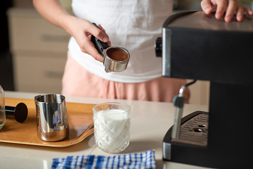 Woman using small home coffee maker to brew her own espresso as home barista