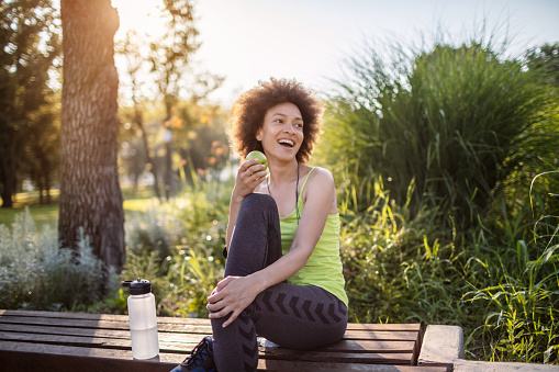 Mixed race woman resting in a park after jogging and eat her healthy snack.