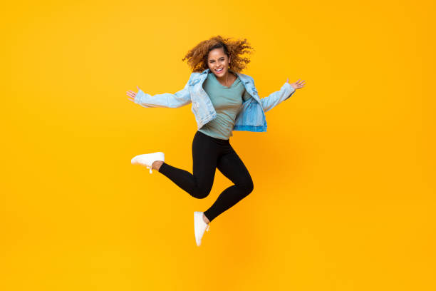Happy energetic smiling young African-American woman jumping Happy energetic smiling young African-American woman jumping isolated on yellow background bouncing photos stock pictures, royalty-free photos & images