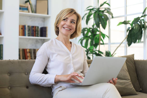 istock Cheerful middle aged woman using laptop while sitting on sofa at home. 1255605872