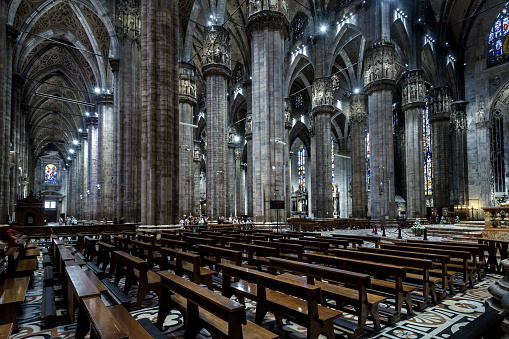 Milan, Italy - May 16, 2017: Interior of large Milan Cathedral or Duomo di Milano. It is great Catholic church, top landmark of Milan. Inside dark Gothic cathedral, panorama of pews and big columns.