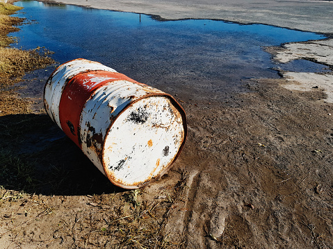 Green rusty metal fuel barrel in abandoned industrial dilapidated buildings.