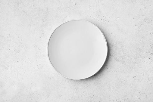 Empty white plate  on white stone table, top view, copy space.