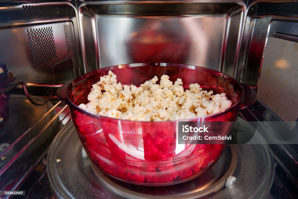 Popcorn prepared in microwave oven. Popcorn prepared in a red plastic microwave dish in a microwave oven. Close-up. Microwave Stock Photo