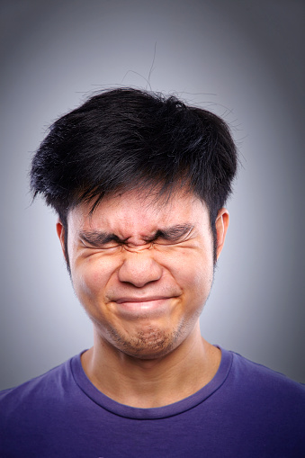 Close up portrait of asian man with grimacing with eyes closed against white gray background.