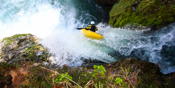 Man in yellow kayak going over a big waterfall. Extreme sports in nature. Danger on river.