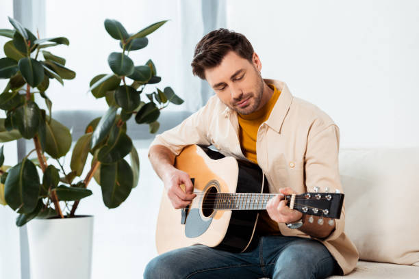 istock Handsome man playing acoustic guitar on couch 1255620481