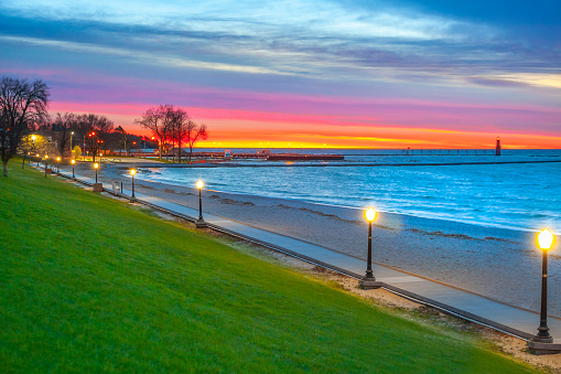 Lighted beach boardwalk with colorful predawn sky, on Lake Michigan's western shore.