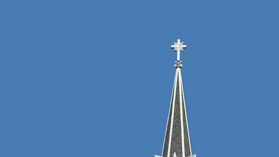 Stainless Steel cross on church steeple isolated on blue sky background.