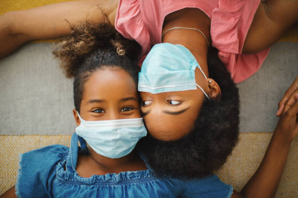 Smiling behind protective face mask. African american mother and daughter lying on the floor, smiling behind protective face mask. Child is looking at camera. woman lying on the floor isolated stock pictures, royalty-free photos & images