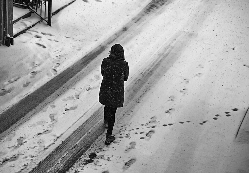 Woman walking in snow on urban street, winter season