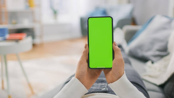 istock Young Woman at Home Lying on a Couch using with Green Mock-up Screen Smartphone. Girl Using Mobile Phone, Browsing through Internet, Watching Content, Chatting in Social Networks with Friends. POV. 1255633818