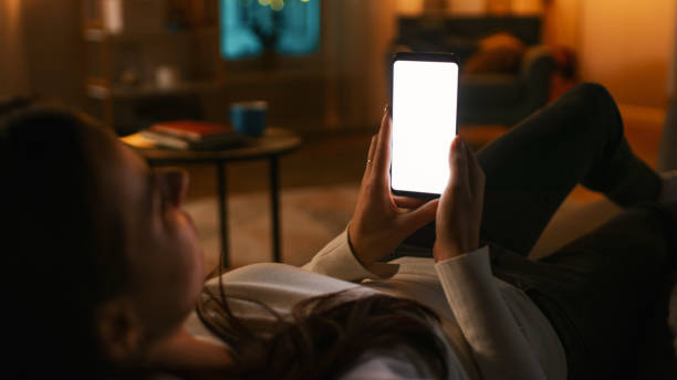 istock Evening at Home: Young Woman Resting on a Couch using with White Mock-up Screen Smartphone. Girl Using Chroma Key Mobile Phone, Internet Browsing, Posting on Social Networks. 1255633831