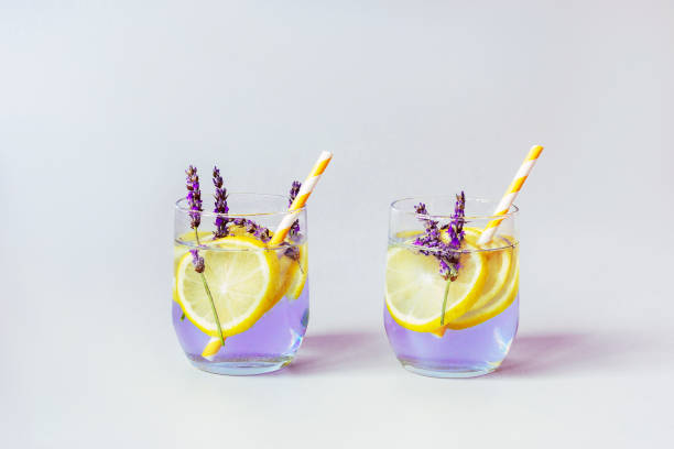 Glasses with lavender lemonade with yellow straws, grey background, close up