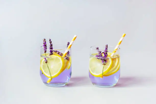 Glasses with lavender lemonade with yellow straws, grey background, close up.