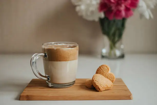 Photo of Transparent cup of dalgona coffee and cookies, bouquet of peonies in background. Cozy morning breakfast