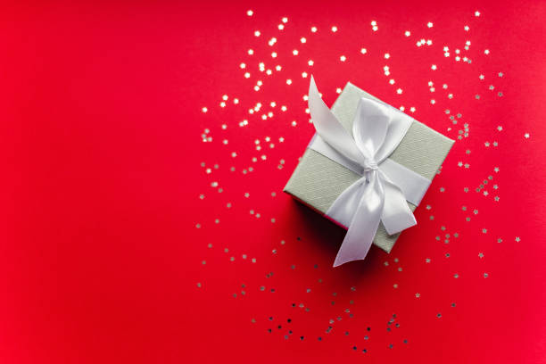 istock Top view Christmas silver gift box with white bow on red background decorated silver stars. Festive present. Copy space 1255636758