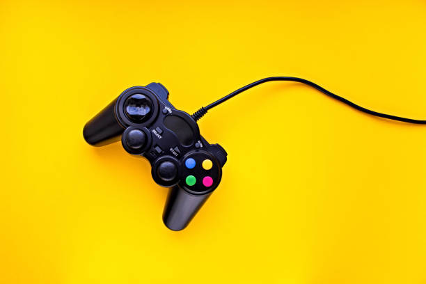 istock Black game controller for a console video game isolated on a yellow background with copy space 1255636775