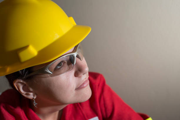 Female Engineer wearing a yellow hard hat, glasses and red coverall
