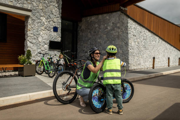 自転車に乗るための彼女の息子を準備若い女性 - セーフティベスト ストックフォトと画像