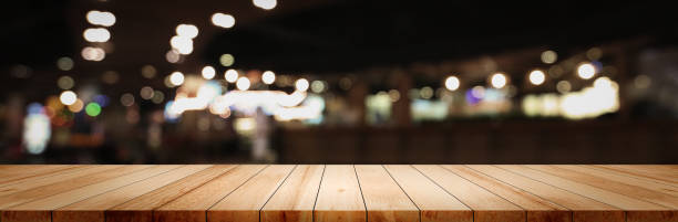 istock Panoramic empty clean wood counter table top on blur street night cafe background use for pub coffee shop montage dark scene, Blurry wide wooden texture shelf bar in luxury restaurant kitchen backdrop 1255651296