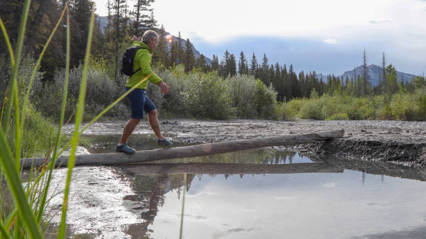 istock Man balances on log and walks across river in the morning 1255651590
