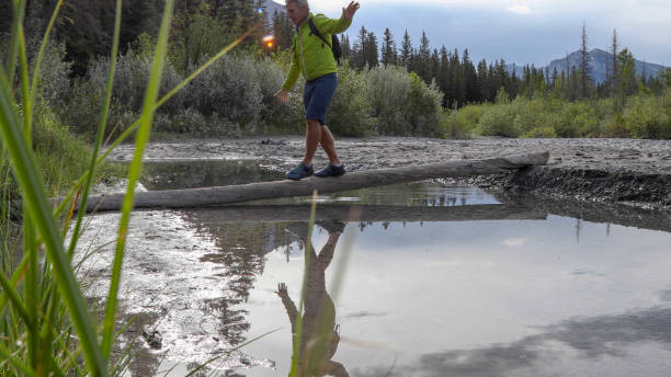 istock Man balances on log and walks across river in the morning 1255651630