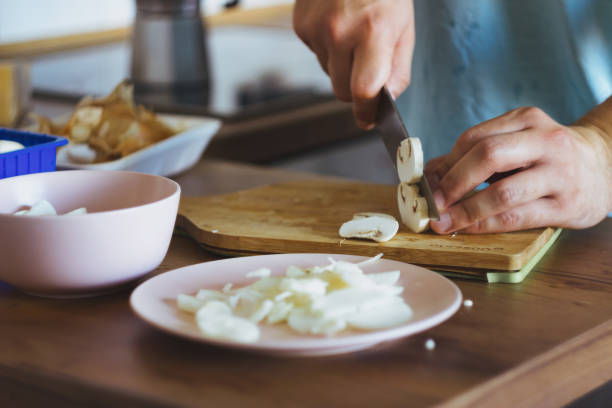 um jovem chef corta cogumelos e cozinha frango. julienne cozinhando - hotel commercial kitchen organic salad - fotografias e filmes do acervo