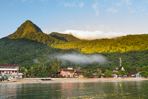 March 5, 2020 - Ilha Grande, Rio de Janeiro, Brazil: Panoramic general view with fishing and tourists colorful boats anchored in tropical paradise Ilha Grande in a sunrise, on back, the little village town with the green rainforest.\n\nIlha Grande (Big Island) is a coastline and a group of small islands and cays located at Rio de Janeiro State in Brazil. A very popular destination for leisure, diving, snorkeling, kite surfing and all kind of water activities. The beauty of the turquoise coastal beaches of Brazil are almost indistinguishable from those of the Bahamas, French Polynesia, Malau, Hawaii, Cancun, Costa Rica, Florida, Miami, Maldives, Cuba, Fiji, Bora Bora, Puerto Rico, Honduras, Thailand, Philippines, or other tropical vacation travel destinations.
