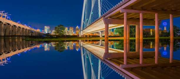 Night lights fill the sky and reflect in the water under several bridges in Dallas, Texas.