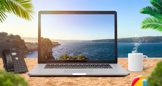 Office on the beach concept, Beach on laptop screen, desk phone with white coffee mug. beautiful beach background.