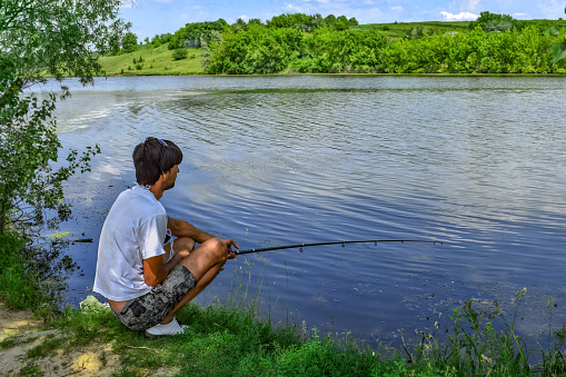 Two boys excitedly pull fish out of lake with fishing pole and net