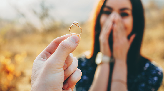 Foto de cerca de un anillo de bodas con diamantes mostrados a la chica mientras ella se sorprende y se cubre la cara con palmas photo