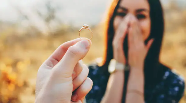 Photo of Close up photo of a wedding ring with diamond shown to the girl while she is amazed and covers her face with palms