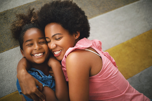 African american mother and daughter lying on the floor, hugging and smiling.