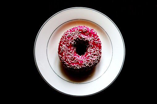 Pink strawberry donut on a white plate - black background