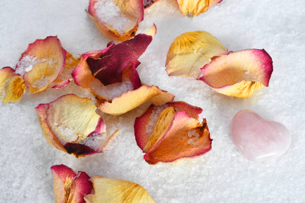 A top view image of white bath salts with dried yellow and red rose petals.