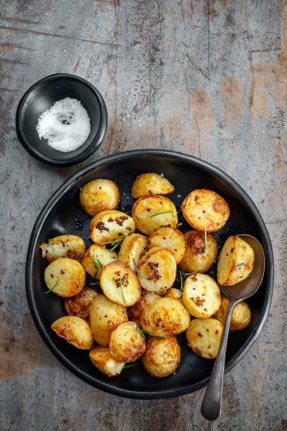 patatas asadas con mostaza integral y romero.  plato negro rústico sobre fondo de madera. - roasted potatoes prepared potato herb food fotografías e imágenes de stock