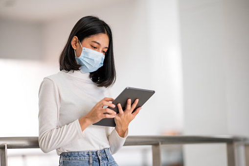 Female graduates wearing a sanitary mask holding a tablet standing at the university