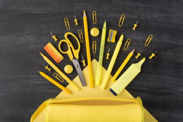 Bright school stationery falling from pencil box concept. Top above overhead view photo of set falling arranged yellow stationery and pencilbox isolated on blackboard