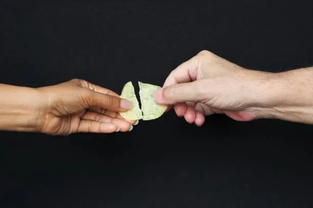 Hands of man and woman breaking same potato chip half for each one. photo isolate on black side view copy space