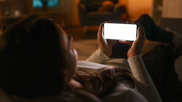 istock Evening at Home: Young Woman Resting on Couch using with White Mock-up Screen Smartphone. Girl Using Chroma Key Mobile Phone in Landscape Horizontal Mode, Internet Browsing, Posting on Social Networks 1255706106