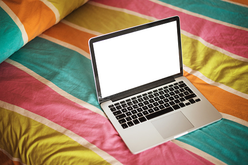 A laptop computer with a blank screen, on a bedroom with colorful sheets