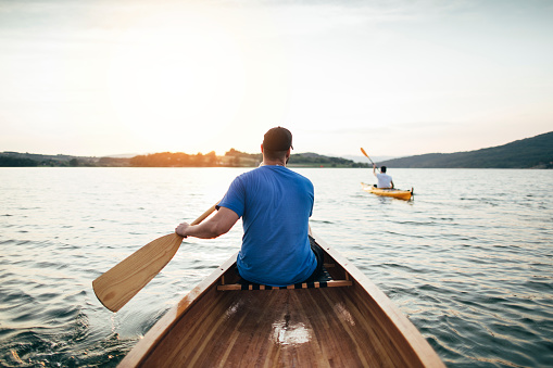 Rear view of men paddling canoe and kayak at sunset lake.