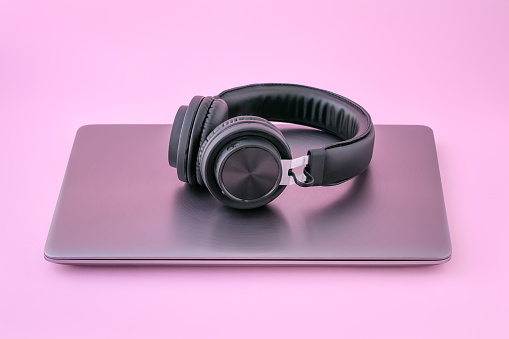 Metal laptop and black headphones on a pink background. Closed notebook with earphones. The concept of self-education