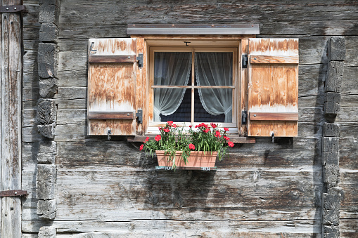 Old wooden shutters worn by the passage of time. The windows reflect the exterior of the house and the interior shows a bed.