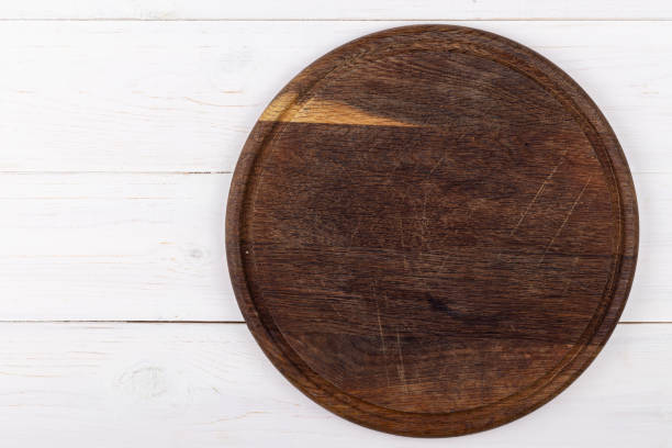 istock Brown round cutting board on a white wooden background. View from above. 1255717078
