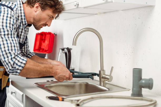 istock Side view of handsome repairman using pipe wrench while fixing kitchen faucet 1255719260